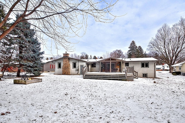 snow covered back of property featuring a deck and a sunroom