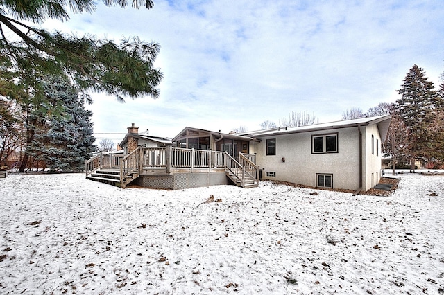 snow covered house featuring a wooden deck and a sunroom