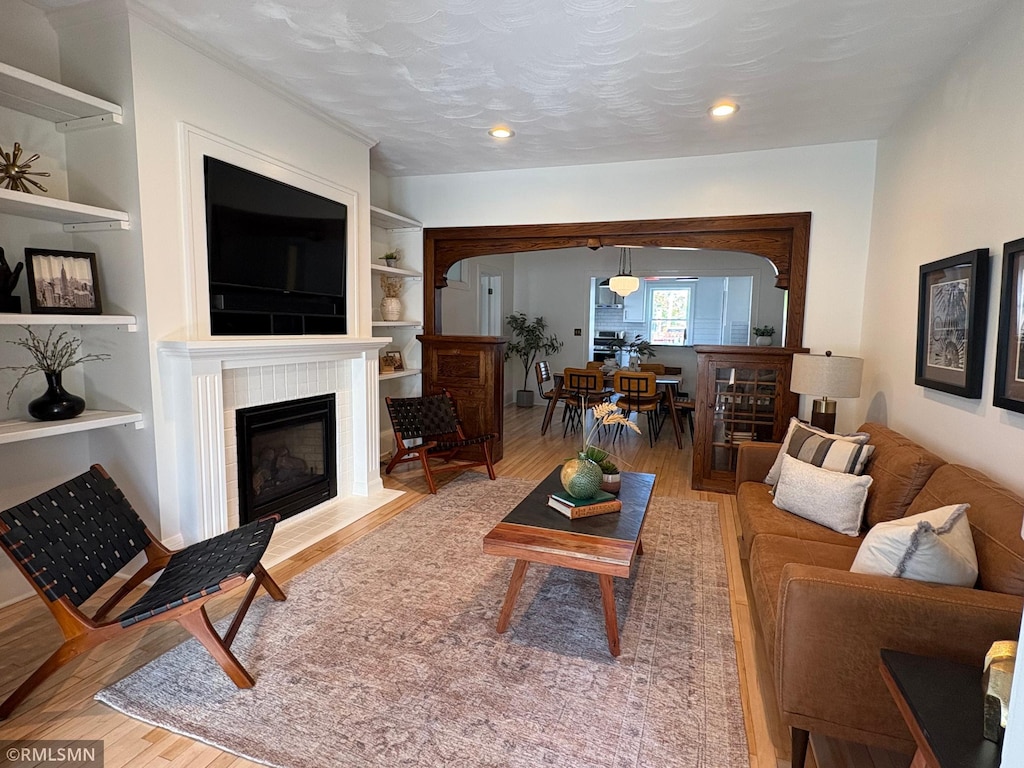 living area with a tile fireplace, recessed lighting, built in features, and wood finished floors
