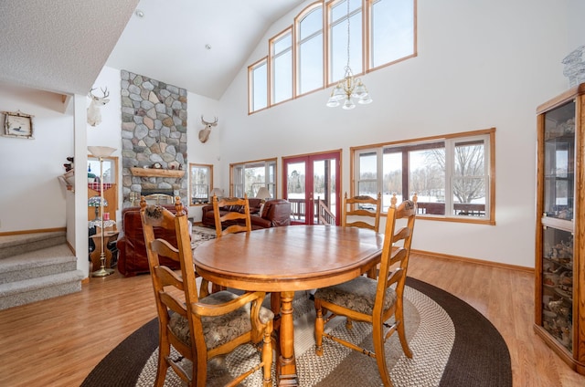 dining space with a stone fireplace, high vaulted ceiling, french doors, and light wood-type flooring