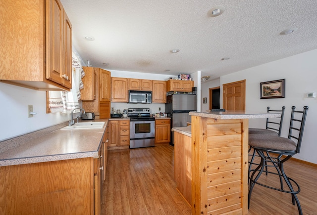 kitchen with sink, appliances with stainless steel finishes, a kitchen island, light hardwood / wood-style floors, and a kitchen bar