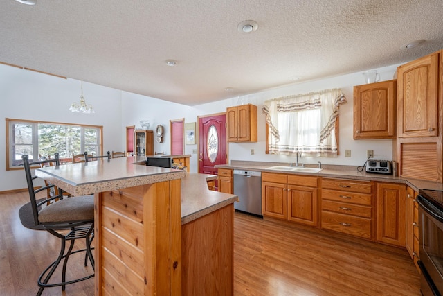 kitchen with sink, a breakfast bar area, a kitchen island, decorative light fixtures, and stainless steel dishwasher