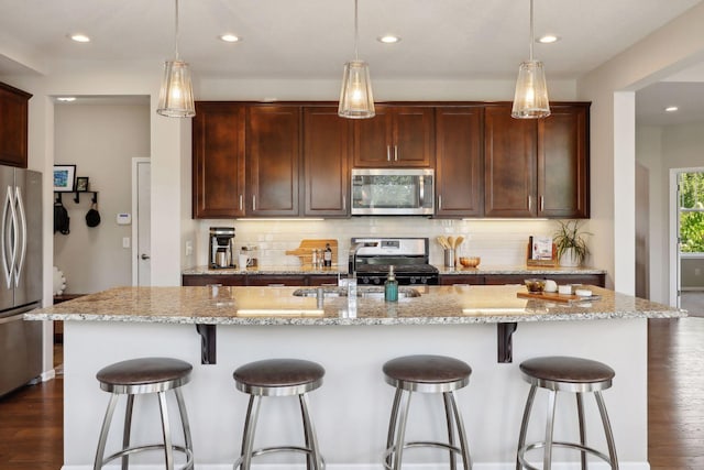 kitchen with stainless steel appliances, dark wood-style flooring, backsplash, and a kitchen breakfast bar