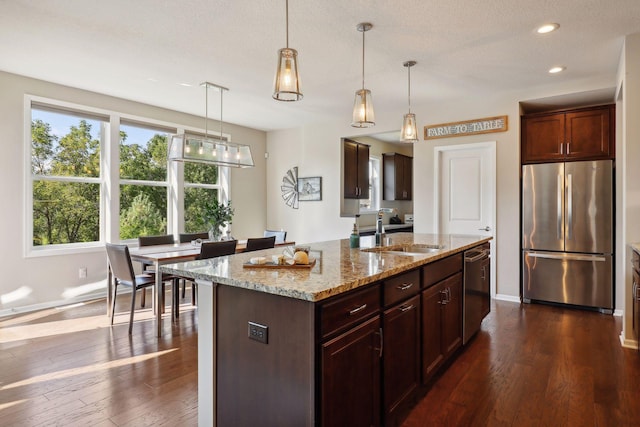 kitchen featuring pendant lighting, dark wood finished floors, appliances with stainless steel finishes, a sink, and light stone countertops