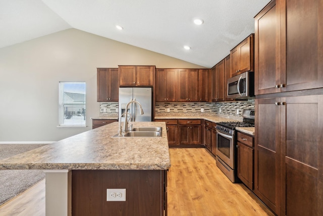 kitchen with sink, light hardwood / wood-style flooring, appliances with stainless steel finishes, an island with sink, and vaulted ceiling