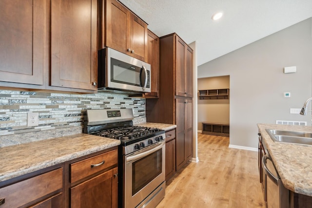 kitchen with lofted ceiling, sink, backsplash, light hardwood / wood-style floors, and stainless steel appliances