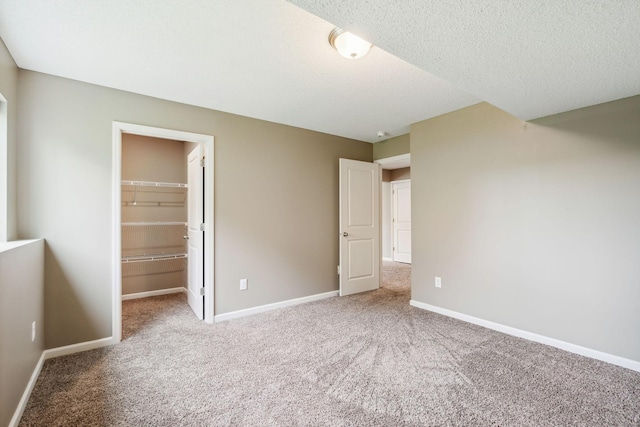 unfurnished bedroom featuring a spacious closet, a closet, a textured ceiling, and carpet