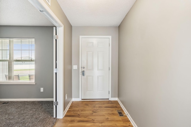 entryway featuring light wood-type flooring, visible vents, baseboards, and a textured ceiling