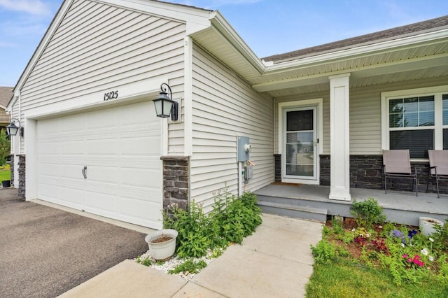 view of exterior entry featuring a porch, a garage, stone siding, and driveway