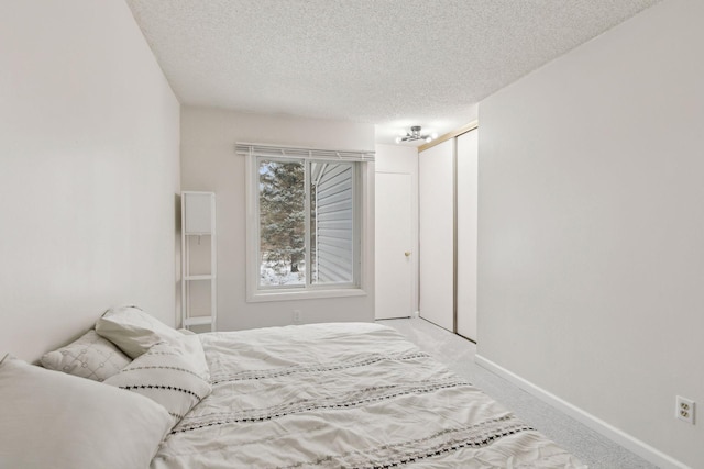 bedroom featuring baseboards, light carpet, a textured ceiling, and a closet