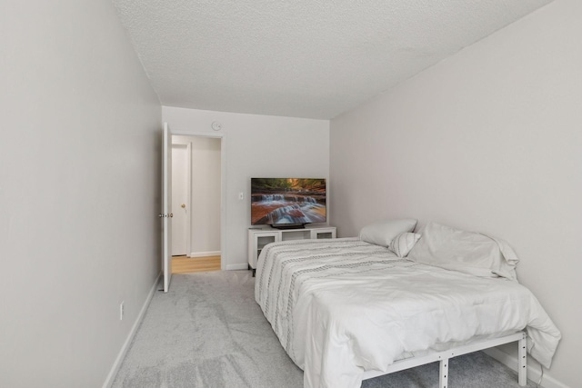 bedroom featuring light colored carpet, a textured ceiling, and baseboards