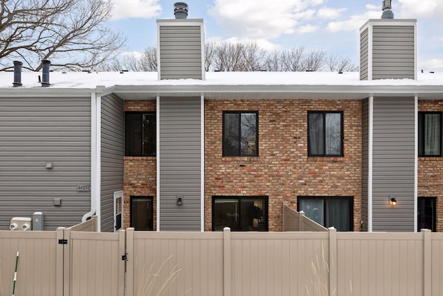 rear view of property featuring a gate, brick siding, a chimney, and fence