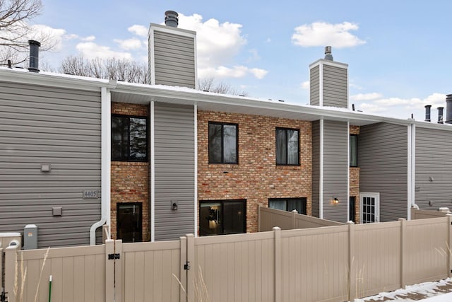 rear view of house with fence private yard, brick siding, and a chimney