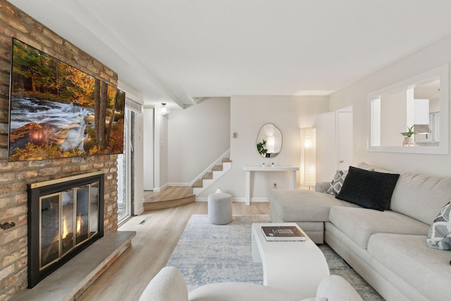 living room with stairs, a fireplace, light wood-type flooring, and baseboards