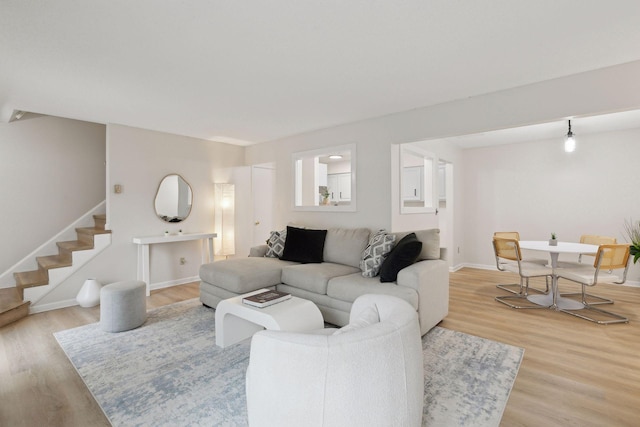 living area with stairway, baseboards, and light wood-style floors