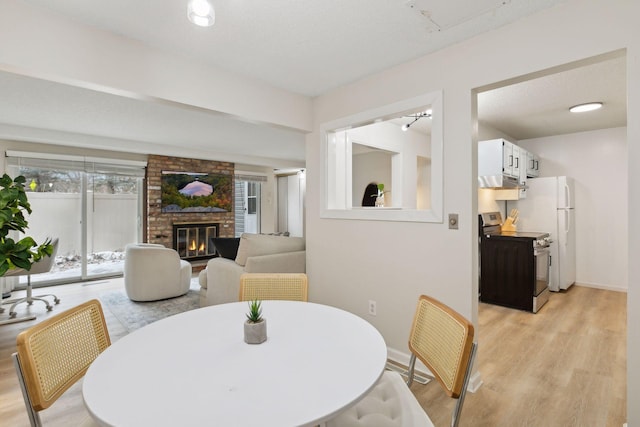 dining area featuring light wood-style flooring, a fireplace, baseboards, and a textured ceiling