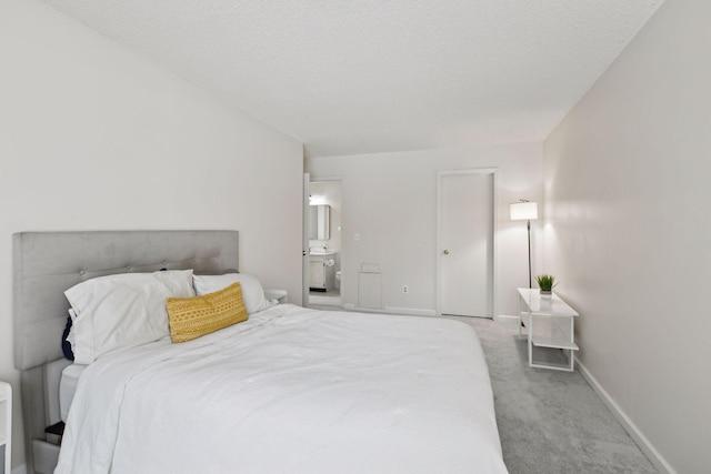 carpeted bedroom with ensuite bath, baseboards, and a textured ceiling