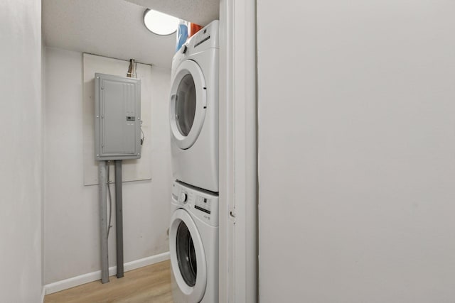 laundry room with baseboards, light wood finished floors, laundry area, electric panel, and stacked washer / dryer