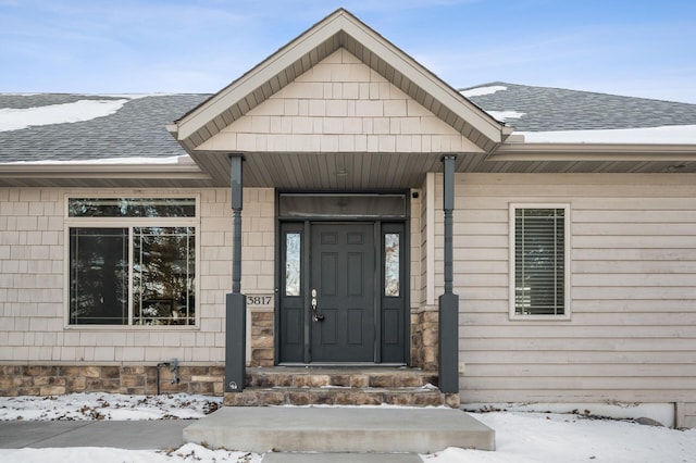 snow covered property entrance featuring a shingled roof