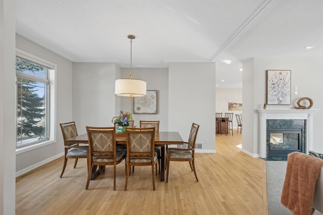 dining area with light wood-style floors, baseboards, crown molding, and a high end fireplace