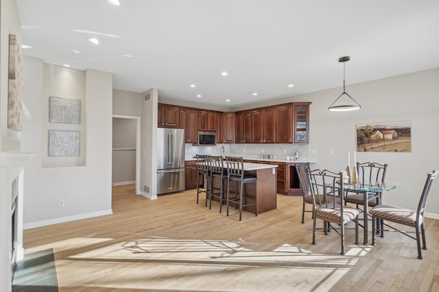 kitchen with a kitchen island, light countertops, appliances with stainless steel finishes, hanging light fixtures, and a kitchen bar