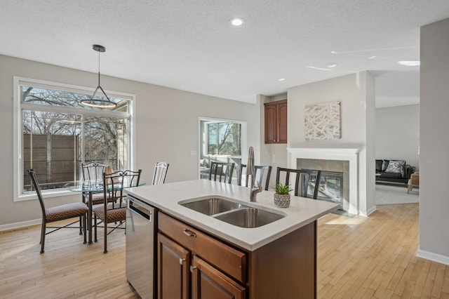 kitchen featuring a center island with sink, dishwasher, hanging light fixtures, light countertops, and a sink