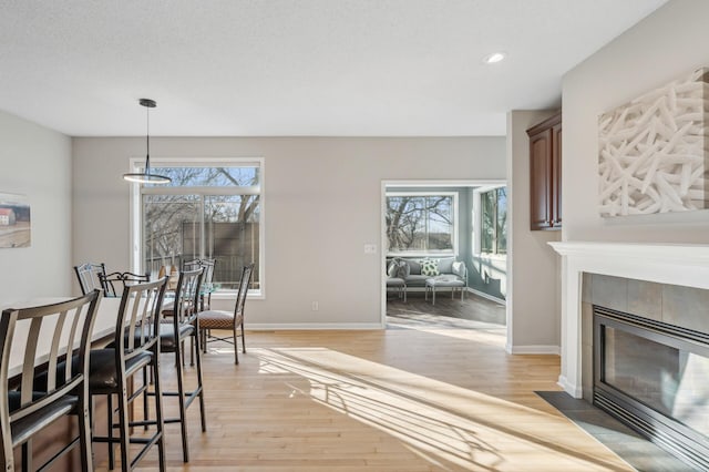 dining room with light wood finished floors, recessed lighting, a tile fireplace, and baseboards