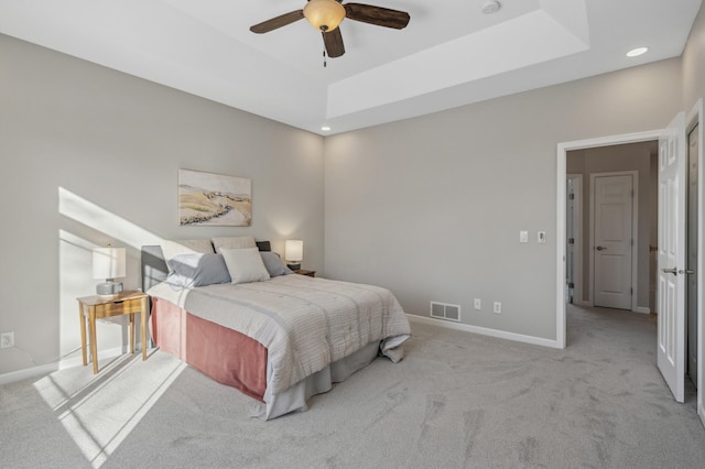 bedroom with light carpet, visible vents, baseboards, a raised ceiling, and ceiling fan