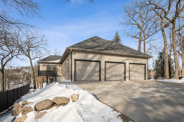 view of snowy exterior with a shingled roof, fence, driveway, and an attached garage