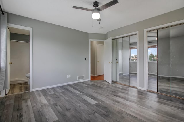 unfurnished bedroom featuring connected bathroom, two closets, light hardwood / wood-style flooring, and a barn door