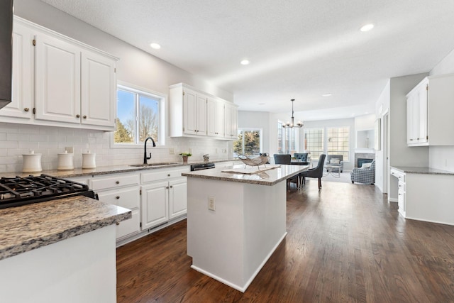 kitchen featuring light stone counters, pendant lighting, white cabinets, a kitchen island, and a sink