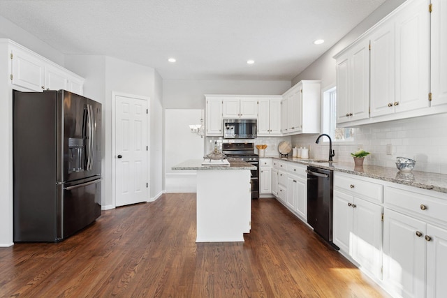 kitchen with light stone counters, a sink, white cabinets, appliances with stainless steel finishes, and a center island