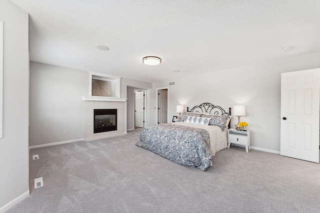 bedroom with light carpet, a glass covered fireplace, visible vents, and baseboards