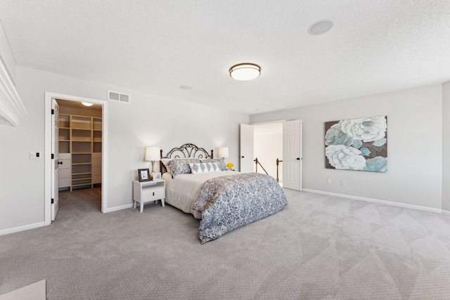 bedroom with light carpet, a walk in closet, visible vents, and baseboards