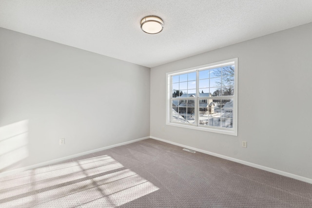 carpeted empty room featuring a textured ceiling, visible vents, and baseboards