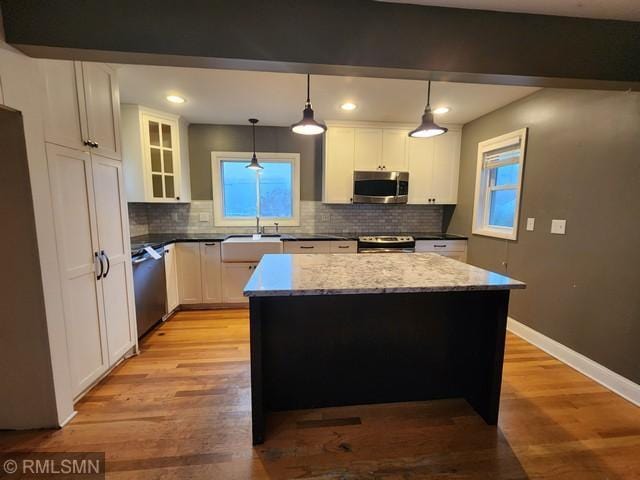 kitchen with pendant lighting, light hardwood / wood-style flooring, appliances with stainless steel finishes, white cabinetry, and a center island