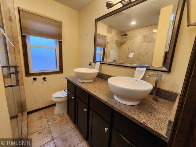 bathroom featuring tile patterned floors, vanity, toilet, and a tile shower