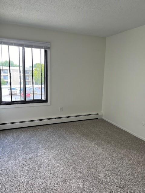 carpeted spare room featuring a baseboard radiator and a textured ceiling