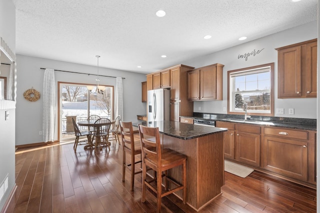 kitchen with sink, hanging light fixtures, a center island, dark hardwood / wood-style flooring, and stainless steel fridge with ice dispenser