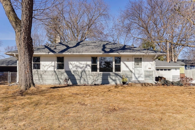 rear view of house featuring a lawn, a chimney, roof with shingles, and fence