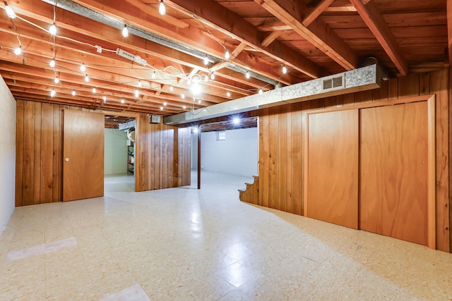 basement with tile patterned floors, wooden walls, visible vents, and track lighting