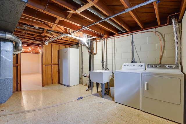 unfinished below grade area with tile patterned floors, washing machine and dryer, freestanding refrigerator, and a sink