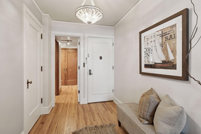 hallway with crown molding, an inviting chandelier, and light hardwood / wood-style floors