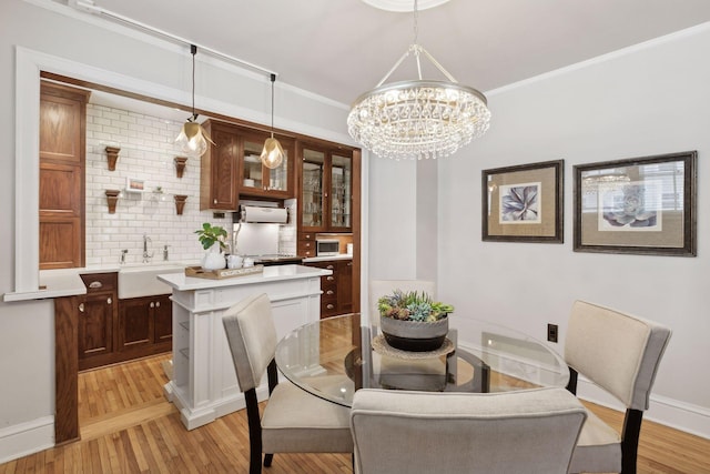 dining area featuring crown molding, sink, a notable chandelier, and light hardwood / wood-style floors