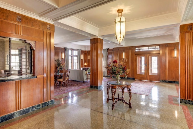 entrance foyer featuring an inviting chandelier, ornamental molding, decorative columns, and wood walls