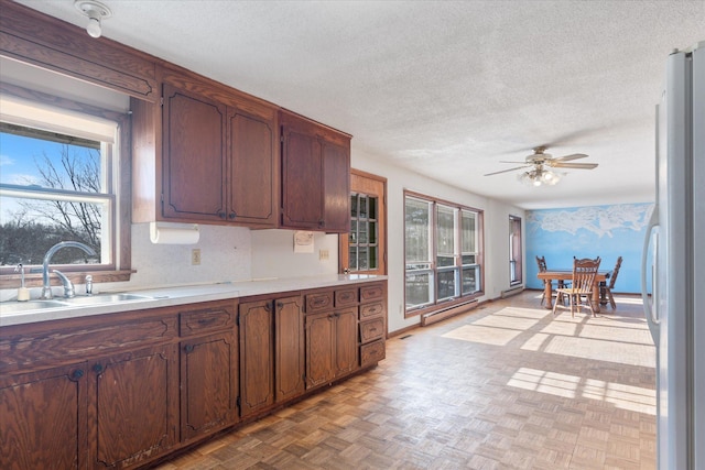 kitchen with a textured ceiling, a sink, a ceiling fan, light countertops, and freestanding refrigerator