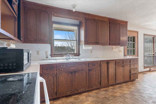 kitchen featuring a textured ceiling, black microwave, light countertops, and a sink