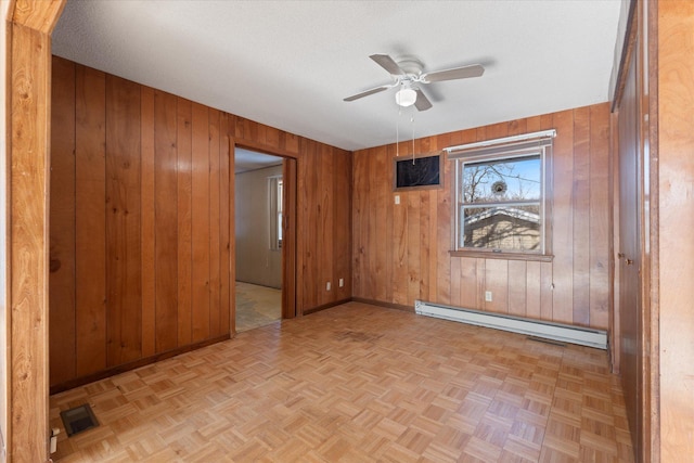 spare room featuring visible vents, baseboard heating, ceiling fan, wooden walls, and baseboards