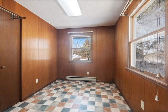 empty room with light floors, a baseboard radiator, wooden walls, and a textured ceiling