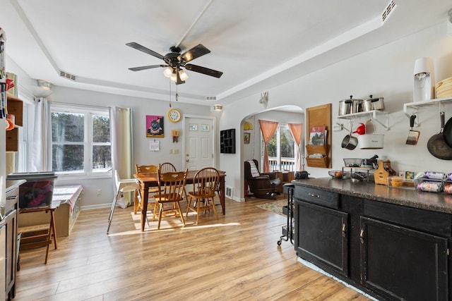 dining room with arched walkways, a raised ceiling, visible vents, and light wood finished floors